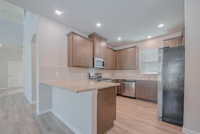 kitchen featuring light wood-style flooring, a peninsula, tasteful backsplash, and stainless steel appliances