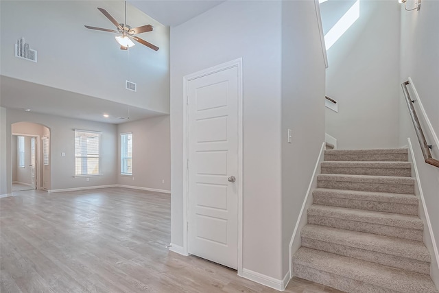 staircase with visible vents, a ceiling fan, a towering ceiling, baseboards, and arched walkways