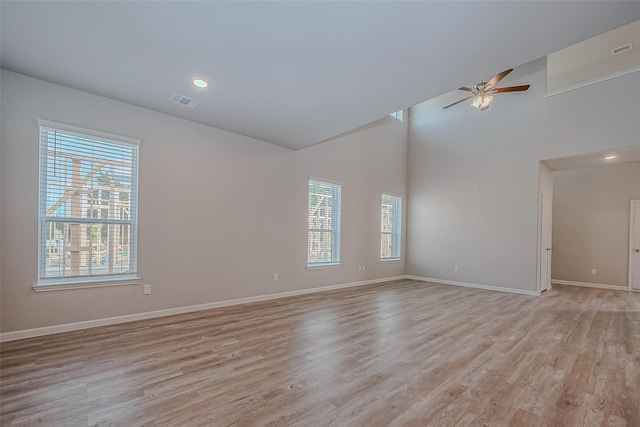 spare room featuring light wood-style floors, baseboards, ceiling fan, and a towering ceiling