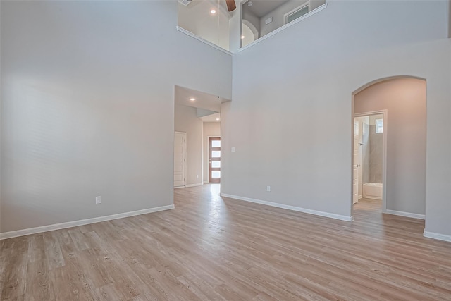 spare room featuring ceiling fan, arched walkways, baseboards, a high ceiling, and light wood-style flooring