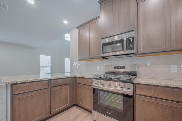 kitchen featuring backsplash, stainless steel appliances, light stone countertops, and a peninsula