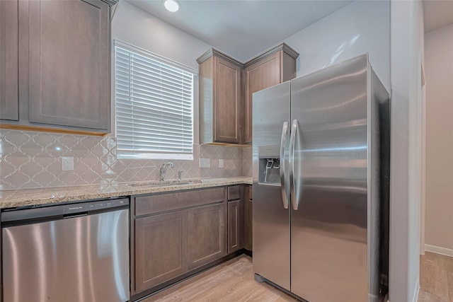 kitchen featuring decorative backsplash, light stone counters, a sink, light wood finished floors, and appliances with stainless steel finishes