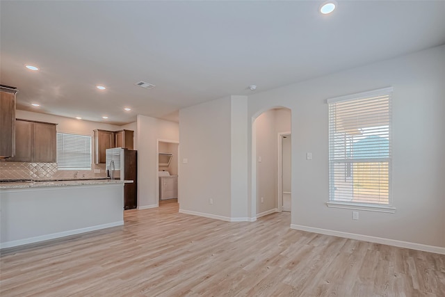 kitchen with washer / dryer, arched walkways, freestanding refrigerator, and light wood-style floors
