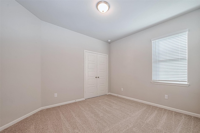 empty room featuring baseboards, light carpet, and vaulted ceiling