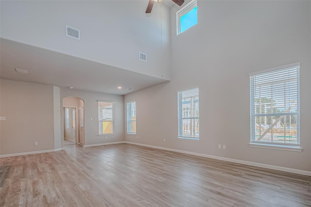 unfurnished living room featuring arched walkways, a ceiling fan, light wood-type flooring, and visible vents