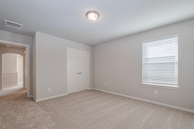 unfurnished bedroom with light colored carpet, visible vents, arched walkways, baseboards, and a closet