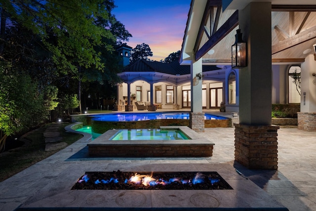 pool at dusk featuring a patio, an in ground hot tub, and an outdoor pool