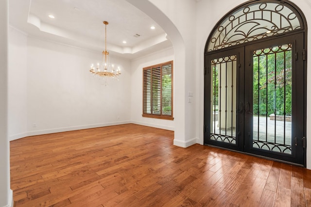 entryway featuring an inviting chandelier, arched walkways, hardwood / wood-style floors, recessed lighting, and a tray ceiling