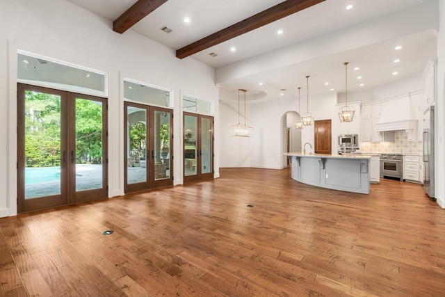 unfurnished living room featuring beam ceiling, french doors, and light wood-style floors