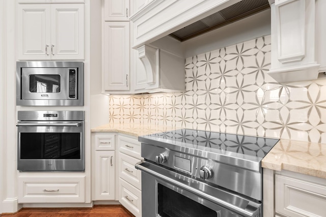 kitchen featuring appliances with stainless steel finishes, tasteful backsplash, light stone counters, custom exhaust hood, and white cabinetry