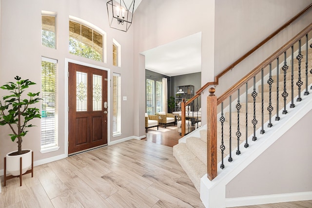 entryway featuring stairs, baseboards, a high ceiling, a chandelier, and light wood-style flooring