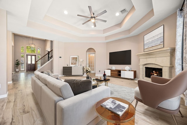 living room featuring ceiling fan, visible vents, arched walkways, a tray ceiling, and a premium fireplace