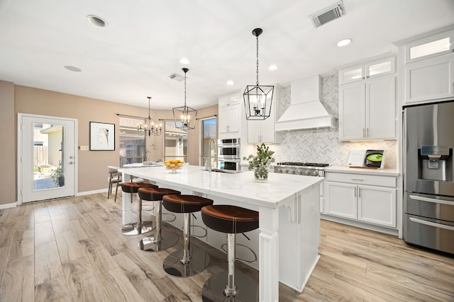kitchen with white cabinets, appliances with stainless steel finishes, decorative backsplash, visible vents, and custom exhaust hood