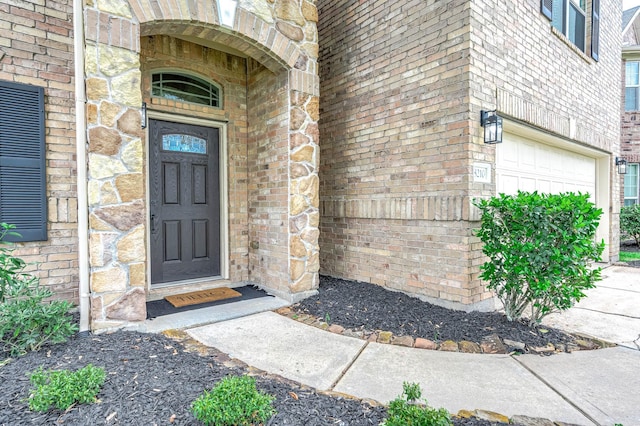 doorway to property featuring an attached garage and brick siding