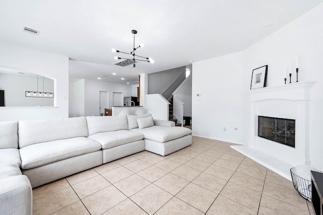living room featuring an inviting chandelier, light tile patterned floors, visible vents, a glass covered fireplace, and stairs