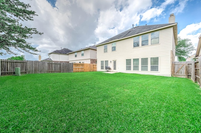 back of house with a yard, a chimney, and a fenced backyard