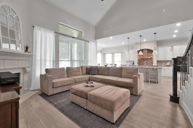 living room featuring stairway, a fireplace with raised hearth, crown molding, high vaulted ceiling, and light wood-type flooring
