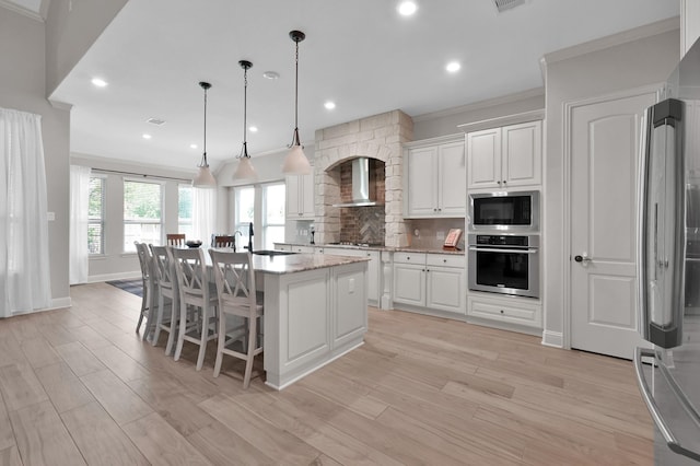 kitchen with appliances with stainless steel finishes, wall chimney range hood, a sink, white cabinets, and ornamental molding