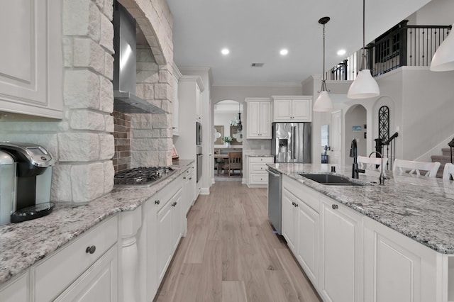 kitchen featuring appliances with stainless steel finishes, a sink, wall chimney exhaust hood, crown molding, and arched walkways