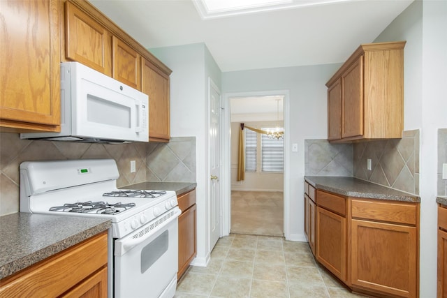 kitchen featuring an inviting chandelier, decorative backsplash, dark countertops, white appliances, and brown cabinets