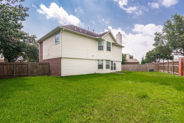 back of house featuring a lawn, brick siding, a chimney, and a fenced backyard