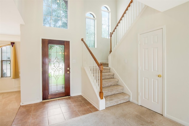 carpeted foyer entrance with baseboards, a towering ceiling, tile patterned floors, and stairway