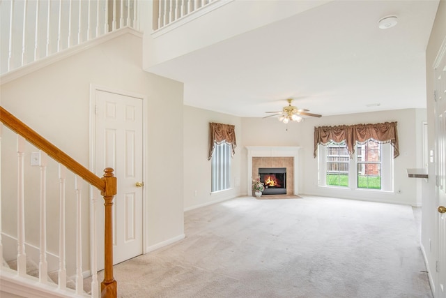 unfurnished living room with carpet floors, stairs, baseboards, a tile fireplace, and a ceiling fan