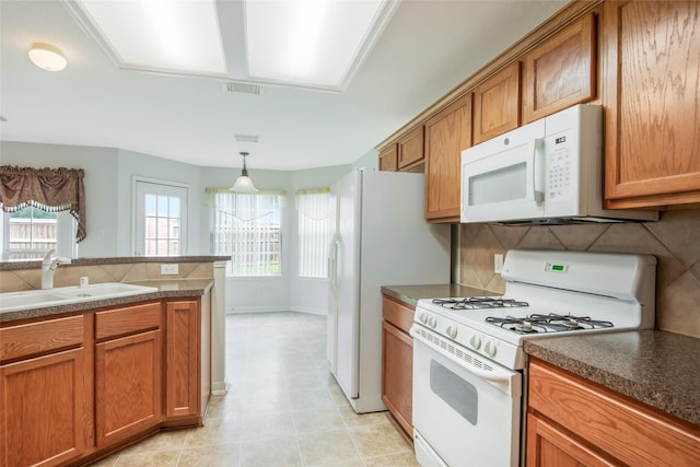 kitchen featuring white appliances, brown cabinets, dark countertops, and a sink
