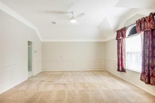empty room with visible vents, wainscoting, lofted ceiling, light colored carpet, and a ceiling fan