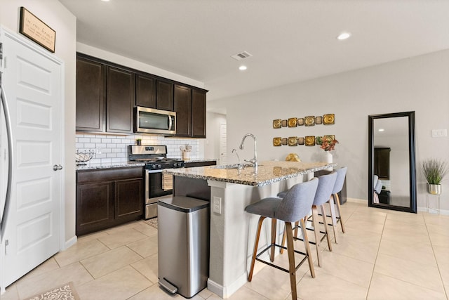 kitchen with light stone countertops, a breakfast bar area, tasteful backsplash, a sink, and appliances with stainless steel finishes