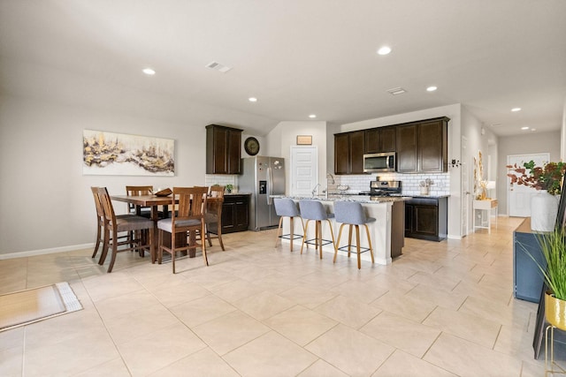 kitchen featuring appliances with stainless steel finishes, decorative backsplash, a kitchen bar, visible vents, and a center island with sink