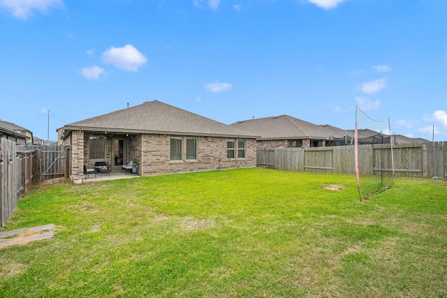 back of property featuring a lawn, a patio area, brick siding, a fenced backyard, and a shingled roof