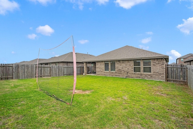 back of house with brick siding, a fenced backyard, a lawn, and a shingled roof
