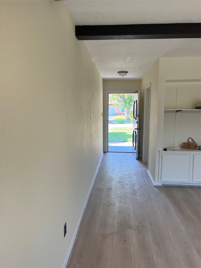 hallway featuring beamed ceiling, baseboards, and light wood-style floors