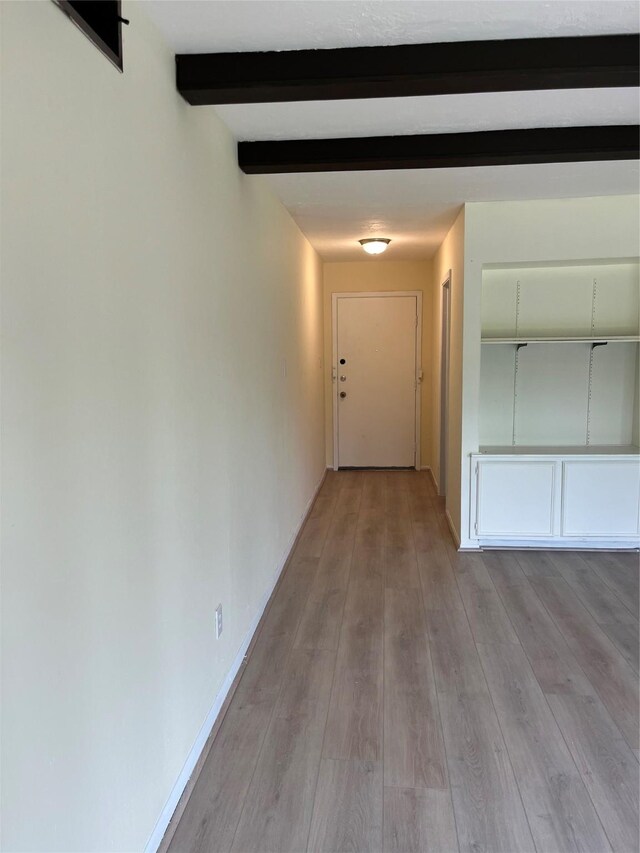hallway with light wood-style floors, beamed ceiling, and baseboards