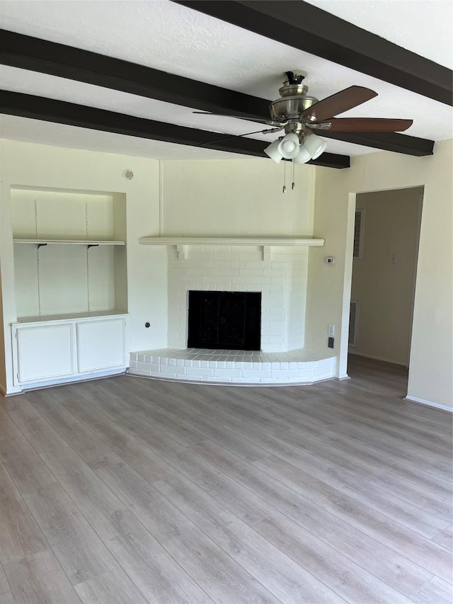 unfurnished living room featuring beam ceiling, a ceiling fan, wood finished floors, baseboards, and a brick fireplace