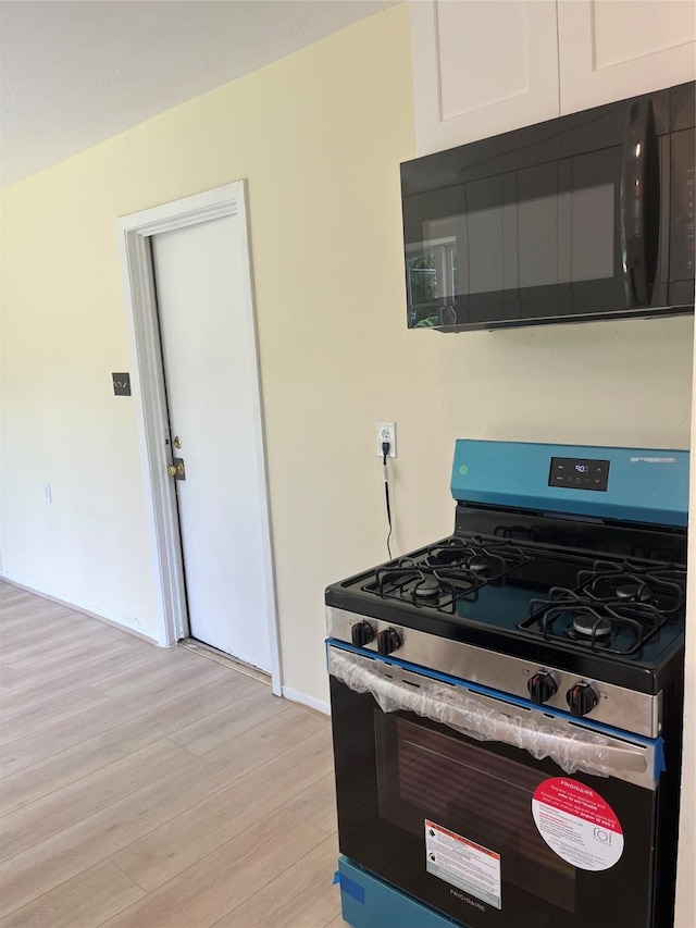 kitchen featuring stainless steel gas stove, black microwave, light wood-style floors, baseboards, and white cabinetry