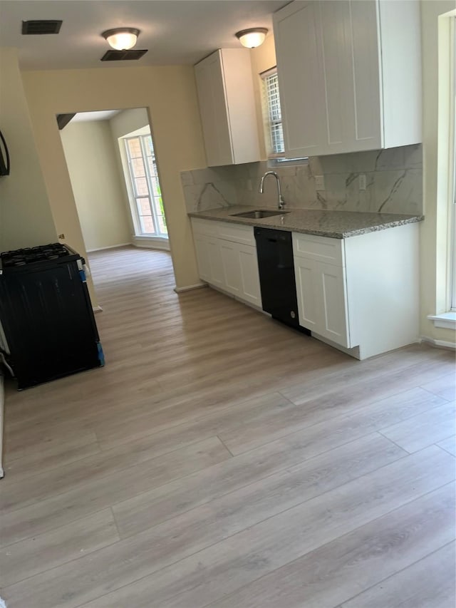 kitchen with black dishwasher, a sink, white cabinetry, and light wood-style floors