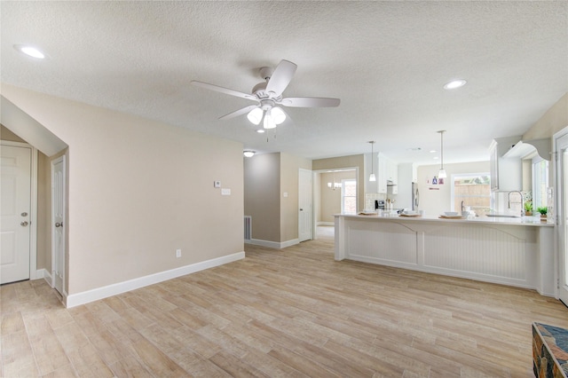 unfurnished living room featuring baseboards, a ceiling fan, light wood finished floors, and a textured ceiling