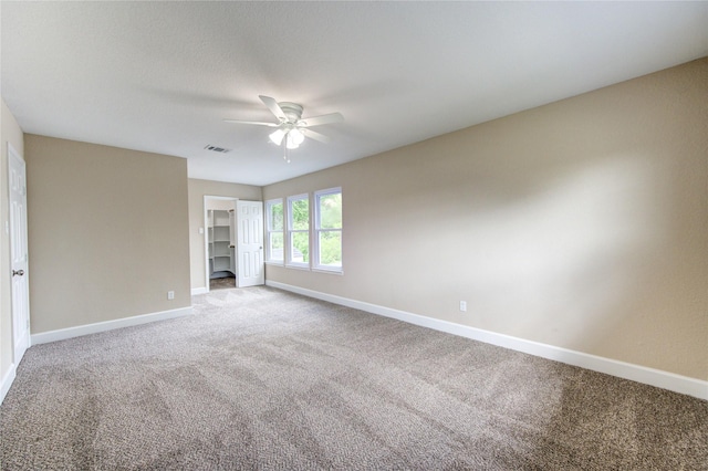 unfurnished bedroom featuring ceiling fan, a walk in closet, carpet, baseboards, and visible vents
