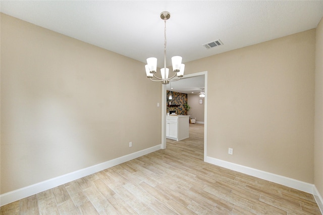 unfurnished room featuring an inviting chandelier, baseboards, light wood-style flooring, and visible vents
