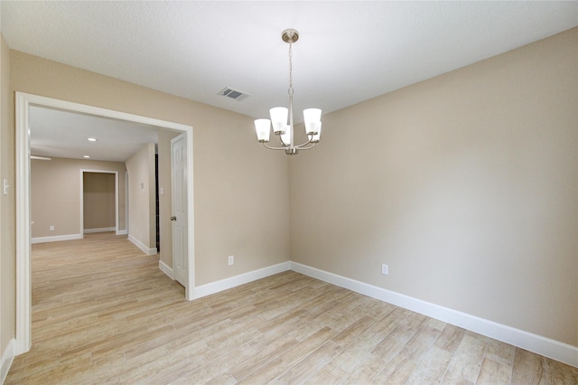 empty room featuring a chandelier, baseboards, visible vents, and light wood-type flooring