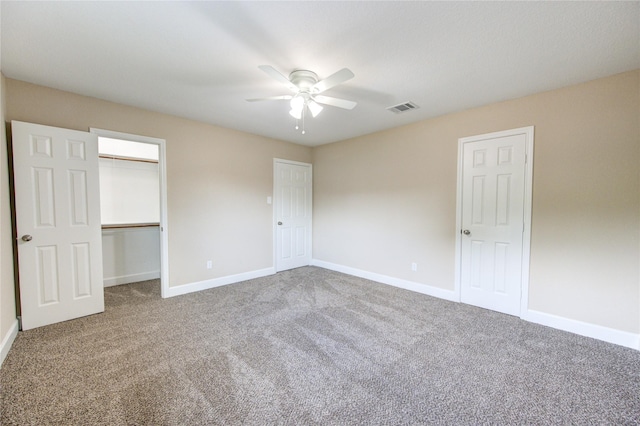 unfurnished bedroom with visible vents, carpet floors, baseboards, ceiling fan, and a spacious closet