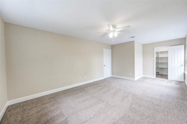 unfurnished bedroom with a walk in closet, carpet floors, a ceiling fan, baseboards, and visible vents