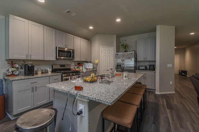 9971 Spring Creek Rd, Cleveland, TX 77327 - kitchen with visible vents, a breakfast bar area, an island with sink, dark wood-style floors, and stainless steel appliances
