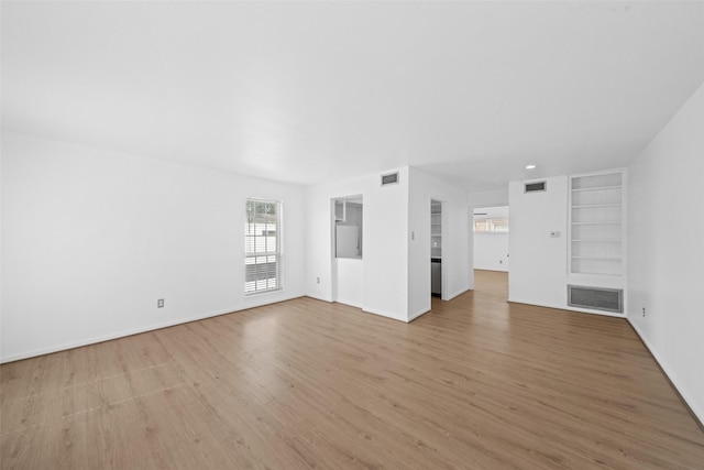 unfurnished living room with visible vents, light wood finished floors, baseboards, and built in features