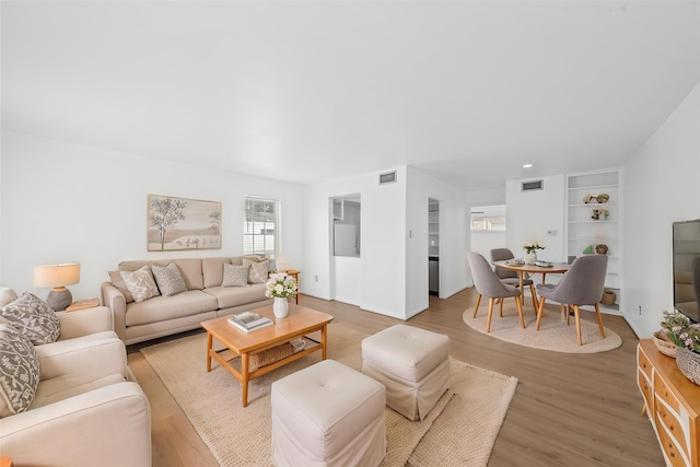 living area featuring visible vents, light wood-style flooring, and built in shelves