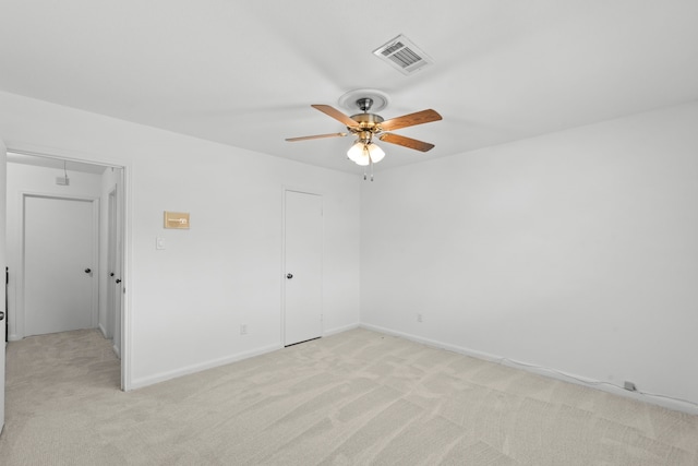 empty room with attic access, visible vents, light carpet, a ceiling fan, and baseboards