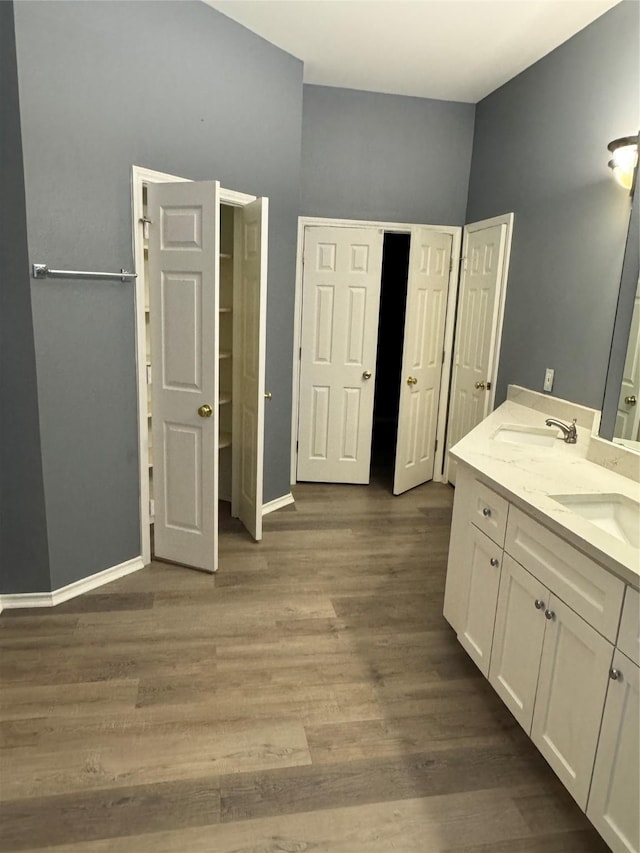 bathroom with double vanity, baseboards, a sink, and wood finished floors