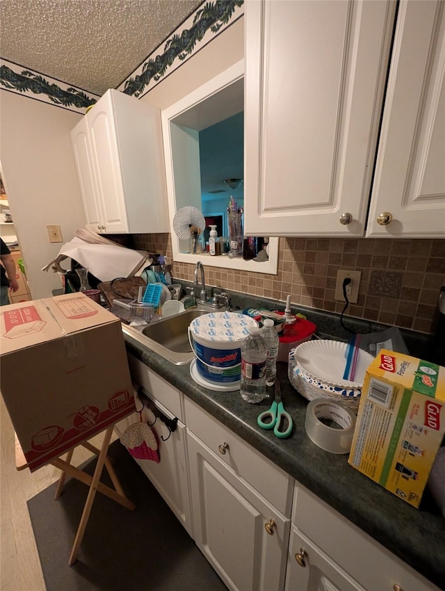 kitchen with a sink, dark countertops, white cabinets, and tasteful backsplash